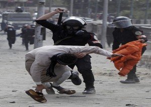 A riot policeman uses his baton on a protester opposing Egyptian President Mursi, during clashes along Qasr Al Nil bridge in Cairo