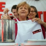German Chancellor Merkel is helped with apron during visit to 'Malteser' mobile kitchen at BBK in Bonn