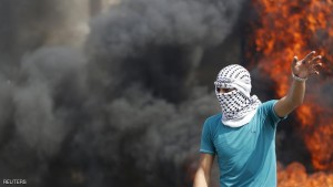 A masked Palestinian protester gestures as smoke rises from a burning tyre behind him during clashes with Israeli troops in the West Bank city of Hebron October 18, 2015. Forty-one Palestinians and seven Israelis have died in recent street violence, which was in part triggered by Palestinians' anger over what they see as increased Jewish encroachment on Jerusalem's al-Aqsa mosque compound. REUTERS/Mussa Qawasma