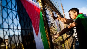 RAMALLAH, WEST BANK - OCTOBER 18: Palestinians look through a fence adorned with flags and posters next to Betunia checkpoint as they prepare for the release of Palestinian prisoners from Israeli prisons on October 18, 2011 in Ramallah, West Bank. A high-profile prisoner swap, which will see the release of captive Israel Defense Forces soldier Gilad Shalit, began before dawn today. Shalit is to be freed after more than 5 years of captivity in Gaza in an exchange deal which will see the release of 477 Palestinian prisoners in an initial deal with another 550 to be freed after the return of Shalit. (Photo by Ilia Yefimovich/Getty Images)